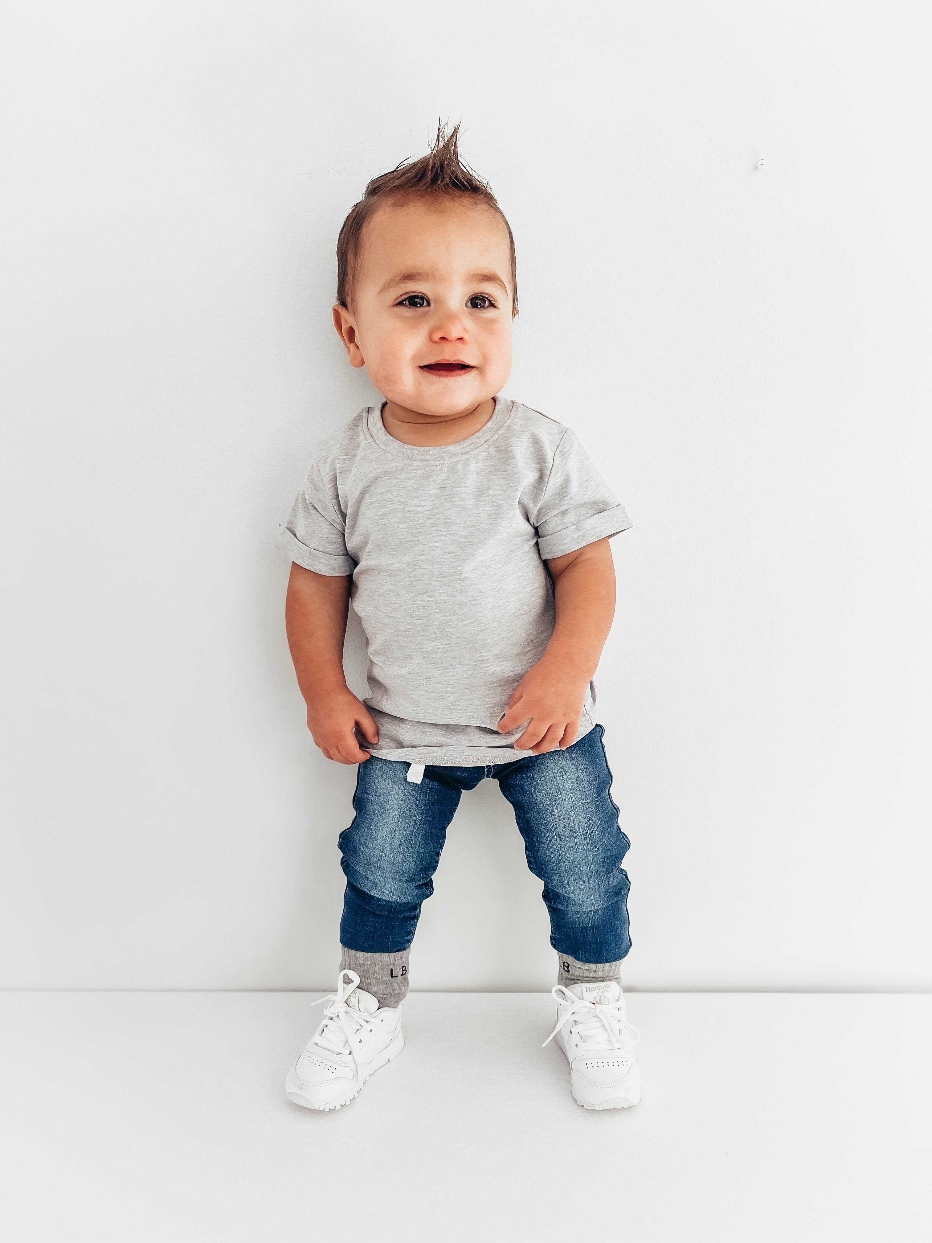 Baby in baby trendy outfit. Baby basic tee in grey and baby denim jeans.